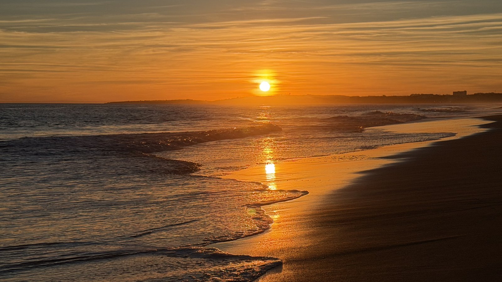 A wide sandy beach with the shoreline curving gently across the frame at low tide.