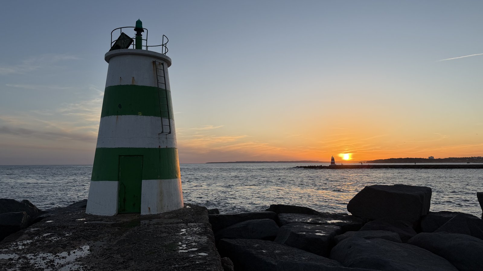 A small lighthouse at the end of a stone pier extending into the sea.