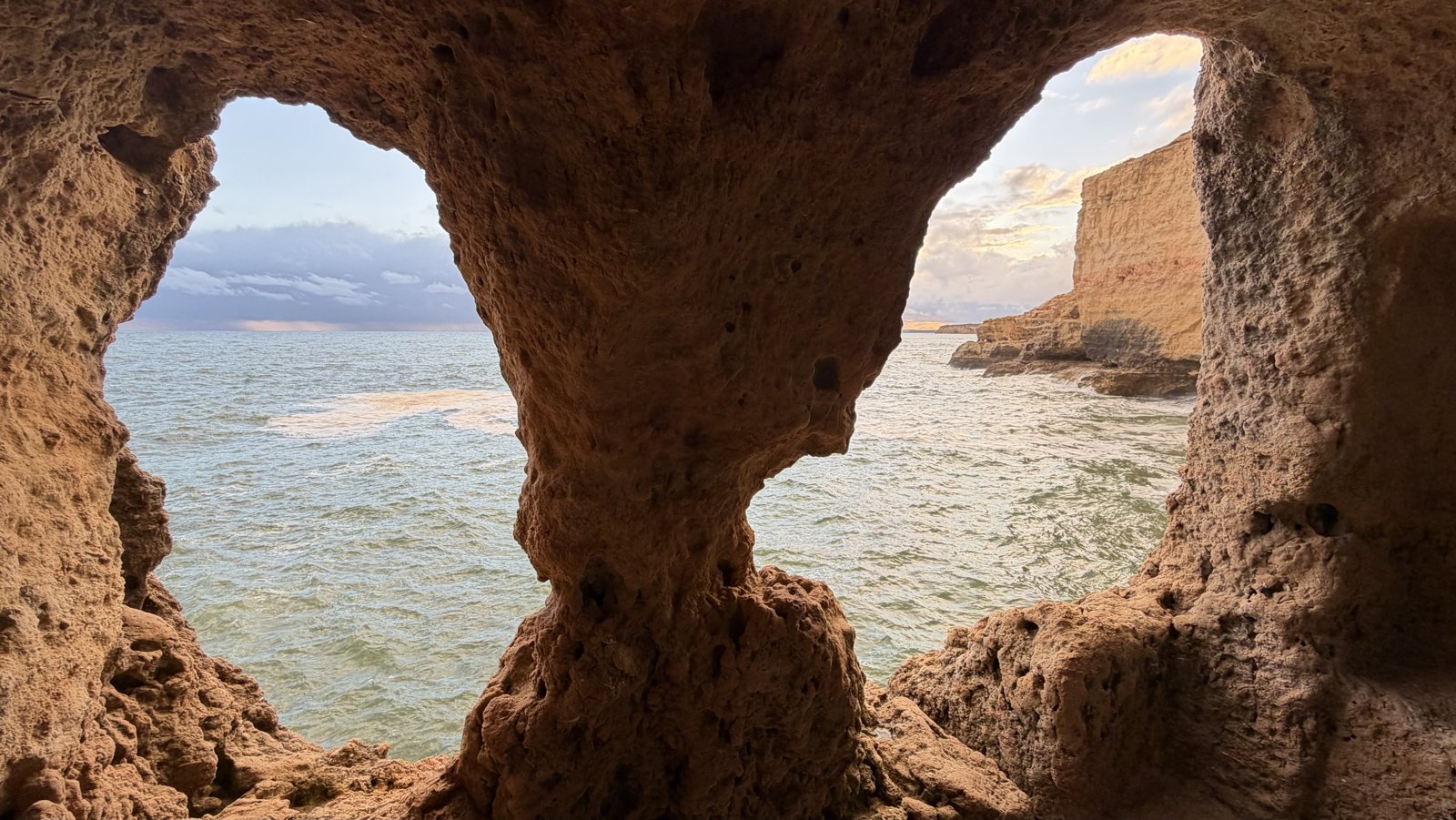 A view of the sea framed by the dark mouth of a coastal cave.