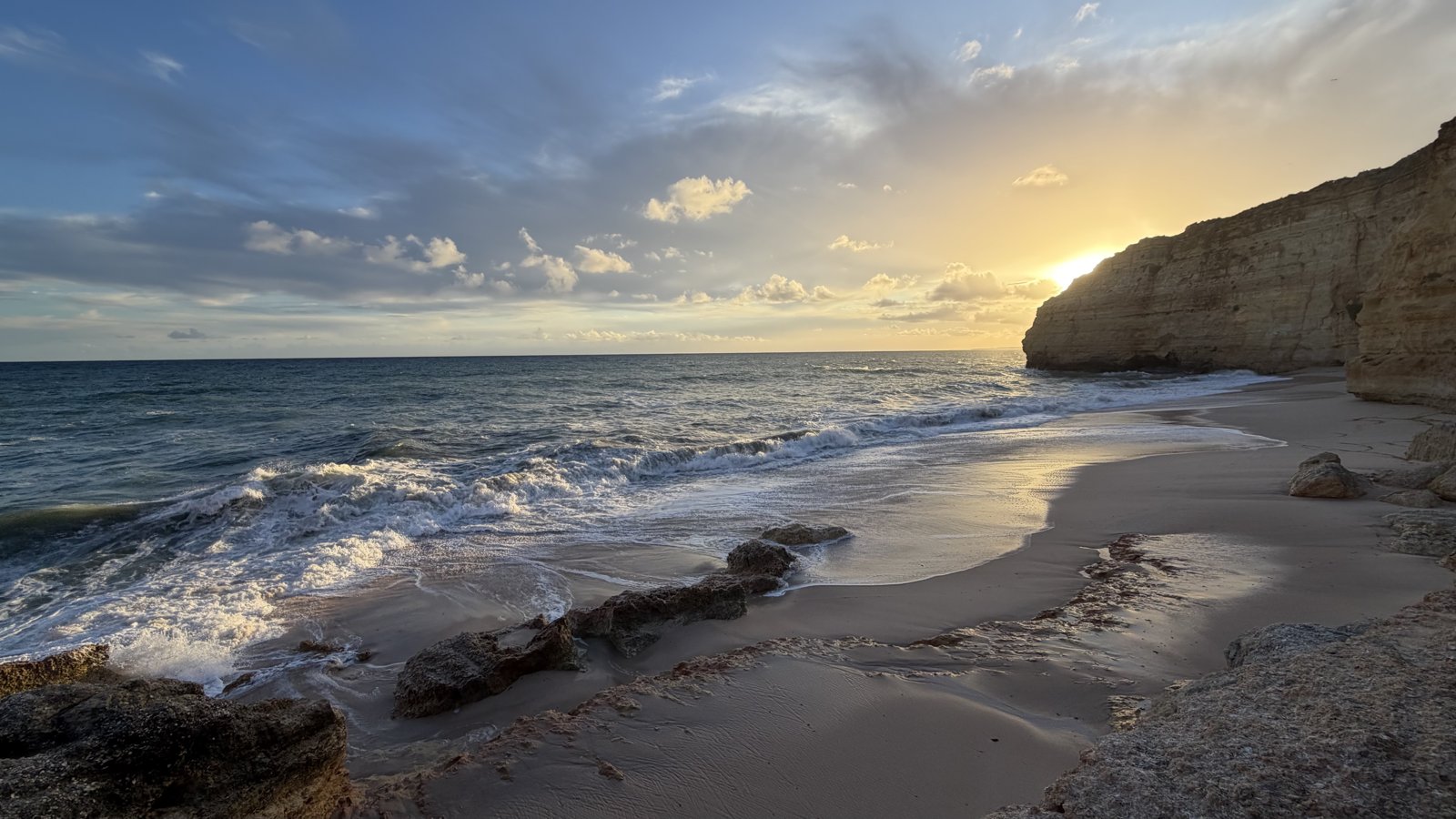 Rock formations on a beach in low, warm side light from the setting sun.