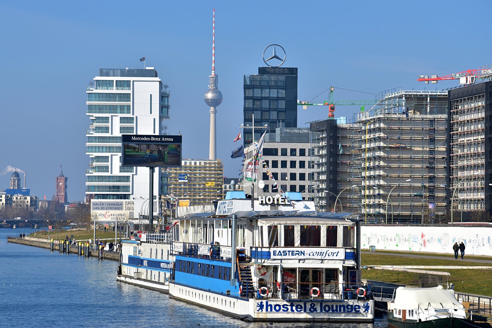 A river boat passing under a bridge, with a modern city skyline behind it.